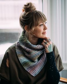 a woman wearing a multicolored knitted cowl sits in front of a window