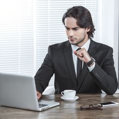 a man sitting at a table in front of a laptop computer with his hand on his chin