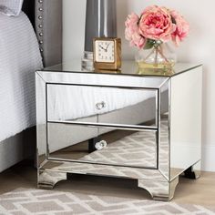 a mirrored nightstand table with a clock and pink flowers on it in front of a bed