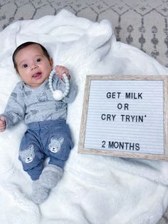 a baby laying on top of a white blanket next to a sign that says get milk or cry tryn't 2 months