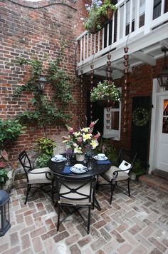 an image of a table and chairs in the middle of a brick patio with flowers on it