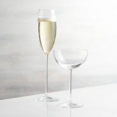 two champagne flutes are sitting next to each other on a white countertop, one is half full and the other half empty