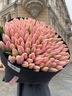 a bunch of pink tulips sitting on top of a black hat in front of a building