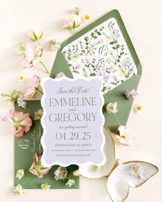 wedding stationery with flowers and envelopes on the table next to it is an envelope that says, save the date emmeline greory