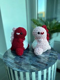 two small crocheted stuffed animals sitting on top of a table next to a potted plant