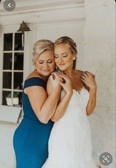 two brides hugging each other in front of a white building with windows and doors