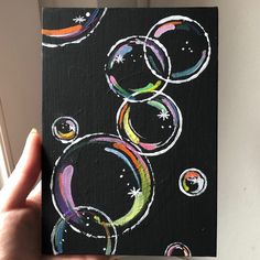 a hand holding up a black and white painting with colorful bubbles on the outside of it