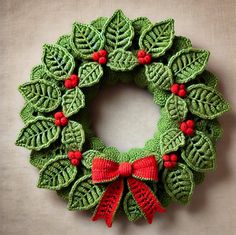 a crocheted christmas wreath with red bows and green leaves on the front, hanging on a wall