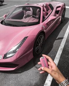 a pink sports car parked in a parking lot next to a person holding a cell phone