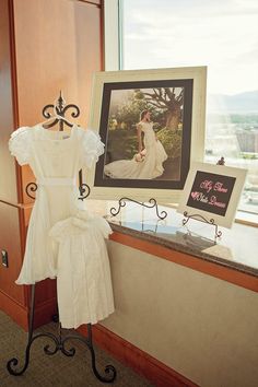 a wedding dress is on display in front of a window with a framed photo and sign