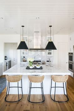 two stools sit at the center of a kitchen island with white marble countertops and black pendant lights