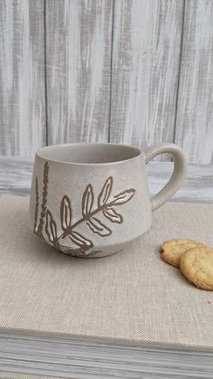 a cookie sitting on top of a table next to a coffee cup with leaves painted on it