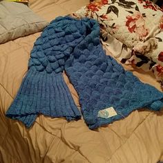 a blue knitted sweater laying on top of a bed next to pillows and blankets