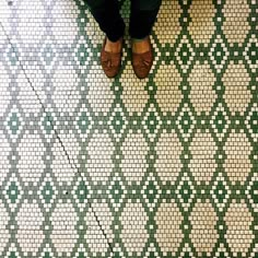 a person standing in front of a green and white tiled floor with brown shoes on it