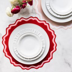 three white plates with red scalloped rims on a marble countertop next to a bouquet of flowers