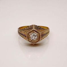 a gold ring with a diamond in the center on a white surface, it has an intricate design and is surrounded by filigree leaves