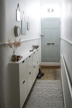 a narrow hallway with white cabinets and a gray door in the center, along with a rug on the floor