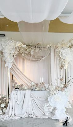 an elegant wedding setup with white flowers and draping on the ceiling, along with black high heel shoes