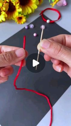 two hands are making something out of yarn and wood skewers on a table with sunflowers in the background