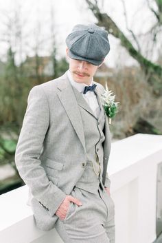 a man in a suit and hat leaning against a wall with his hands on his hips