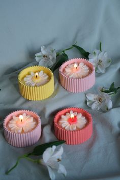 four small pink and yellow candles sitting on top of a white sheet next to flowers