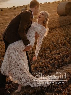 a bride and groom kissing in a field with hay bales behind them at sunset