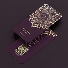 two purple and gold business cards sitting on top of each other with an intricate design