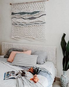 a white bed topped with lots of pillows next to a wall hanging above it's headboard