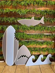 three surfboards and two fish are in front of a wooden wall with moss growing on it