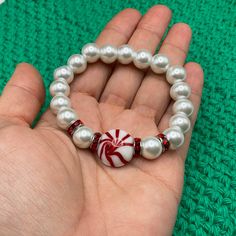 a hand is holding a bracelet with candy canes and white pearls on the beads