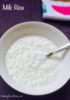 a bowl of milk with a spoon in it on a purple table cloth next to a napkin