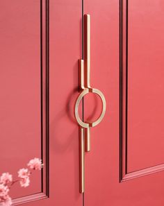 a door handle on a red door with pink flowers in the foreground and a gold ring hanging from it