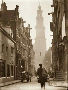 an old black and white photo of a man walking down the street in front of a clock tower