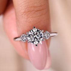 a woman's hand holding a three stone diamond ring