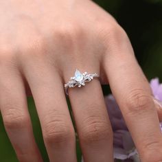 a woman's hand with a ring on her finger and flowers in the background