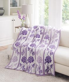 a living room with a white couch and purple flowered blanket on top of it