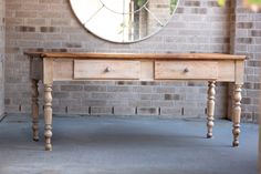 a wooden table sitting in front of a brick wall with a round mirror above it