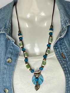 Colorful Turquoise Patina and Bronze charm woven on 1mm Bronze Leather cord with a Bronze Leaf charm and Blue Bone. Mated with bright blue Pony, Peridot color agate, white Bone and Bronze beads come together on two 1mm bronze leather cords with a decorative bronze "S" clasp for closing. Charm is 1" round and total length of necklace is 22". No lead or nickel used. Please use the Last On, First Off approach. Stones discolor with lotions, perfumes, hairspray, sweat, chlorine, even some soaps, and will break if dropped. Hippie Green Jewelry With Colorful Beads, Adjustable Green Necklace For Everyday Use, Everyday Adjustable Green Necklace, Beaded Bohemian Necklaces, Bohemian Multicolor Necklaces For Everyday, Multicolor Bohemian Necklaces For Everyday Use, Bohemian Turquoise Necklace With Adjustable Cord, Bohemian Beach Jewelry With Heart Beads, Beach Green Jewelry With Heart Beads