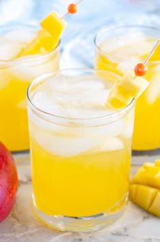 two glasses filled with lemonade and ice on top of a white table next to sliced oranges