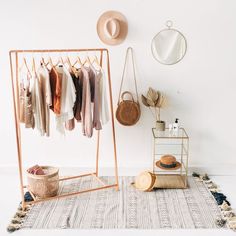 a clothing rack with clothes hanging on it next to a hat and other items in front of a white wall