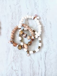 Soft, serene, cozy, and beachy. Beautiful beige, white, caramel, brown, and ecru in these mixed medium stack bracelets. Several white Howlite, White Turquoise, Quartz, and more. Gemstone beads in different sizes and colors. Creamy alabaster ethical bone beads, matte sea shells, white and natural coconut disk beads, rustic antique beads, and African recycled glass. Mix in with an array of mixed metals, and cluster accents of mixed gemstone beads including pearls. Unique and stunning. The item/s p White Beaded Beachy Bracelet, Beachy White Beaded Bracelet, Adjustable White Beaded Beachy Bracelets, Beachy Adjustable White Beaded Bracelets, Brown Beaded Bracelets With Natural Stones For Beach, Brown Natural Stones Beaded Bracelets For Beach, Brown Natural Stone Beaded Bracelets For Beach, Earthy Natural Stone Beaded Bracelets For Beach, White Bohemian Bracelets For Vacation