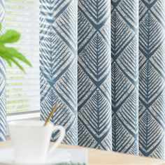 a coffee cup sitting on top of a table next to a window covered in blue and white patterned curtains