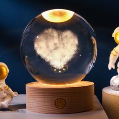 two small figurines stand next to a snow globe with an image of the moon in it