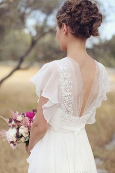 the back of a woman's wedding dress, with flowers in her hair and holding a bridal bouquet