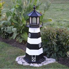 a black and white lighthouse sitting in the middle of a garden next to some bushes