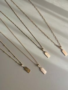 four different necklaces with tags on them sitting on a white surface, one is gold and the other is silver