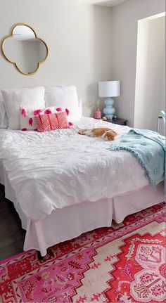 a white bed with pink and blue pillows on top of it next to a rug