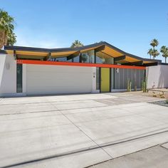 a modern house with palm trees in the foreground and an orange, yellow, and grey roof