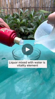 someone pouring water into a glass bowl with a red bottle in it and another hand holding a plastic container