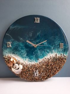 a clock that is on the side of a wall with sand and shells in it